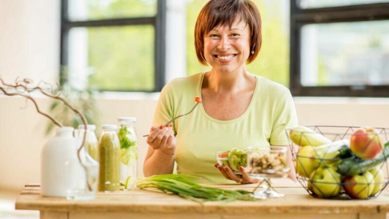 Smiling lady at kitchen table eating healthy salad